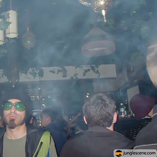 Man in Sunglasses and Hat Stands Among Nightclub Crowd